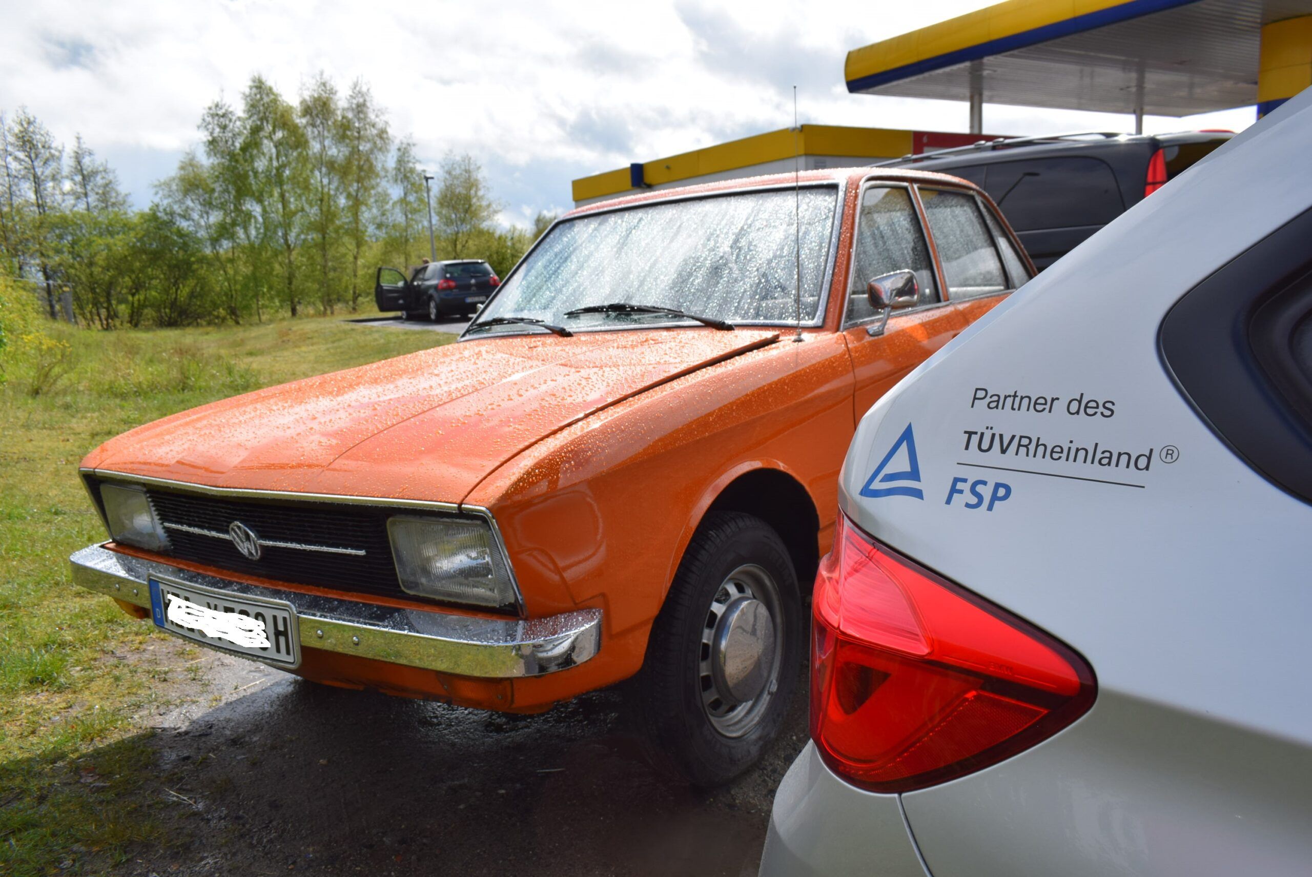 Oranger VW Oldtimer bei einer Begutachtung, daneben ein Fahrzeug mit TÜV Rheinland Partner-Logo – Oldtimergutachten